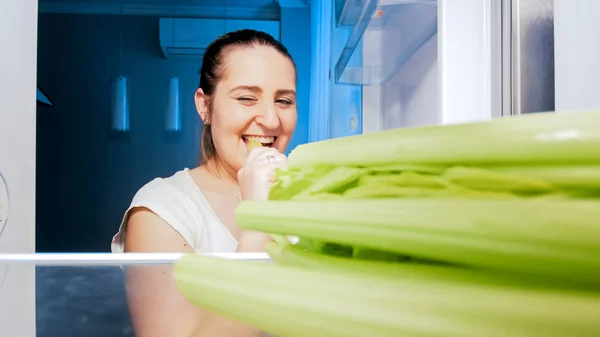 Potret wanita tersenyum yang makan seledri di dapur pada malam hari — Stok Foto
