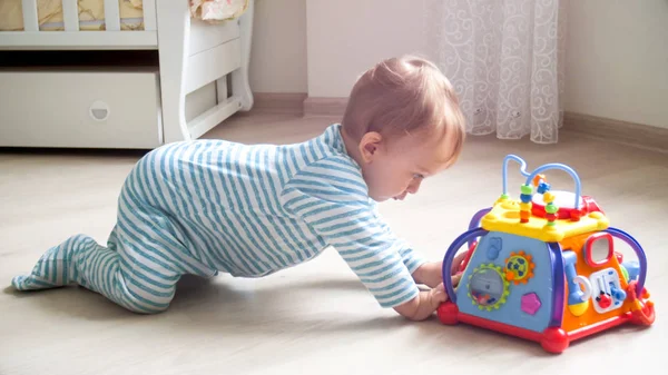 Ładny 1 roku życia chłopca czołgał się na podłodze w kierunku kolorowe zabawki — Zdjęcie stockowe