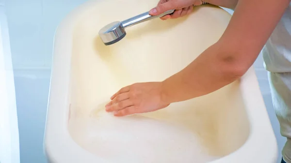 Image rapprochée d'une jeune femme vérifiant la température de l'eau dans une baignoire pour bébé avec une main — Photo