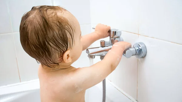 Gros plan image de 1 ans tout-petit garçon essayant d'ouvrir le robinet d'eau dans la salle de bain — Photo