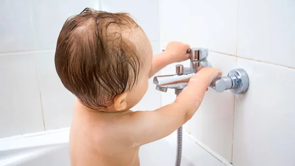 Mignon tout-petit garçon ouvre robinet d'eau lors du lavage dans le bain — Photo