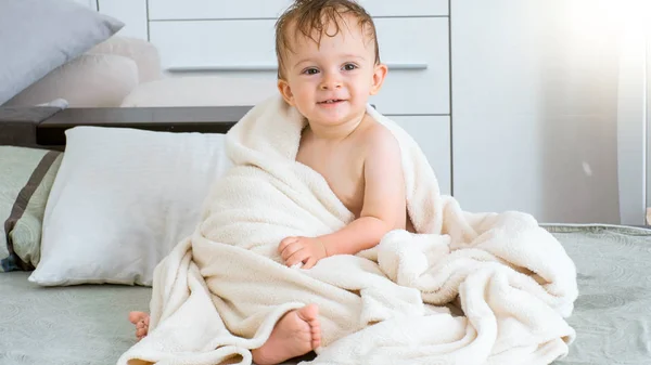 Retrato de menino sorridente bonito depois de tomar banho sentado na cama — Fotografia de Stock