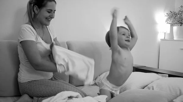 Черно-белый веселый мальчик играет в постели с молодой улыбчивой матерью ночью — стоковое фото