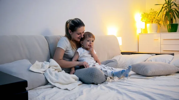 Mulher bonita sentada com seu filho criança na cama à noite — Fotografia de Stock
