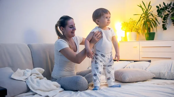 Lindo niño pequeño en pijama con joven madre sonriente en la cama antes de ir a dormir — Foto de Stock