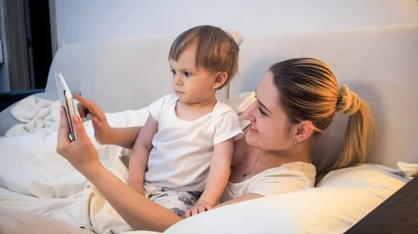 Портрет улыбающейся матери и мальчика, смотрящего мультики на планшете в постели — стоковое фото
