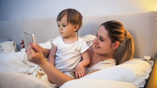 Portrait of smiling young woman with toddler son lying in bed with tablet computer — Stock Photo, Image