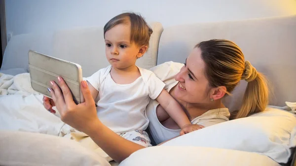 Portrait de jeune mère avec tout-petit fils regardant des dessins animés sur tablette numérique au lit — Photo