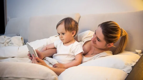 Tonificado retrato de niño lindo acostado con la madre en la cama y viendo dibujos animados —  Fotos de Stock