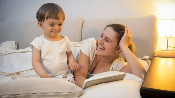 Feliz madre alegre con hijo pequeño acostado en la cama en ngiht —  Fotos de Stock