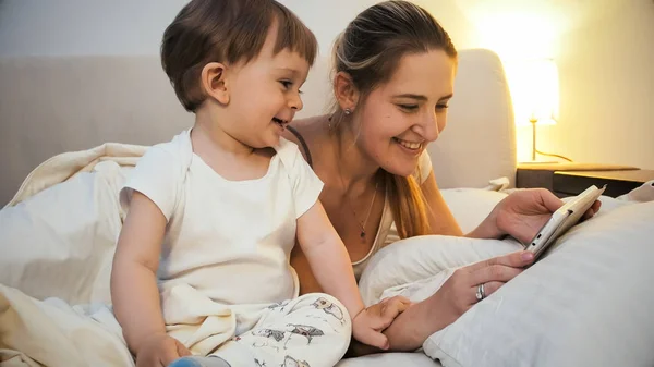 Retrato de feliz madre sonriente jugando en digital con su hijo pequeño antes de irse a dormir — Foto de Stock