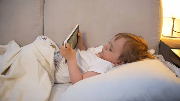 Tablet yatakta çizgi film izlerken çok güzel yürümeye başlayan çocuk portresi — Stok fotoğraf