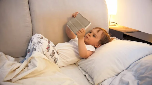 Retrato de niño lindo con tableta digital acostado en la cama — Foto de Stock