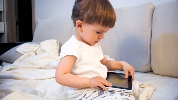 Retrato de niño lindo sentado en la cama y jugando en la tableta digital —  Fotos de Stock