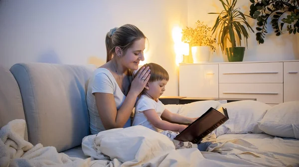 Ładny 2 lat toddler chłopiec czytanie duże historia książki w nocy w łóżku — Zdjęcie stockowe