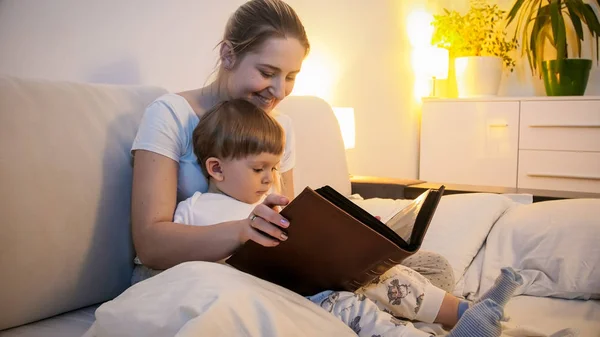 Тонированный портрет улыбающейся молодой женщины, читающей сказку своему сыну перед сном — стоковое фото