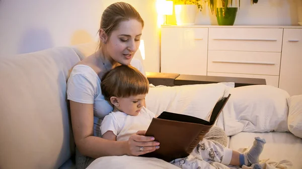 Lindo niño en pijama leyendo cuento de hadas con su madre antes de irse a la cama — Foto de Stock