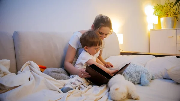 Cute toddler boy looking at big fairytale book with mother before bedtime — Stock Photo, Image