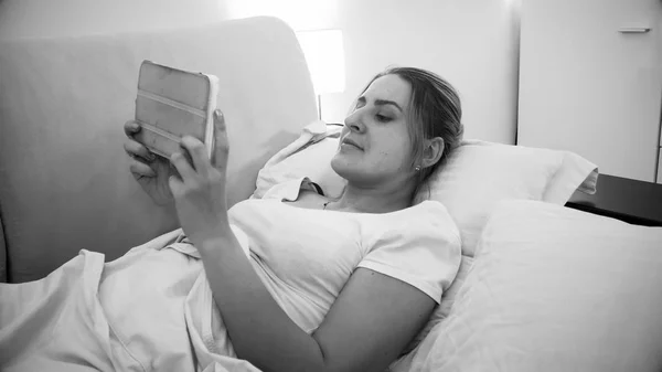 Ritratto in bianco e nero di giovane donna sdraiata con tablet digitale a letto — Foto Stock