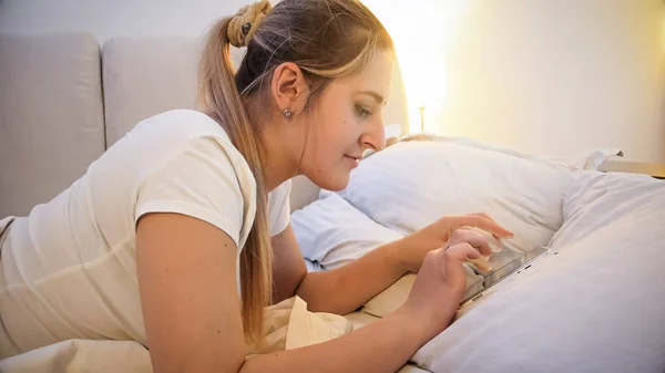 Retrato de mujer joven en pijama escribiendo mensaje en tableta digital por la noche —  Fotos de Stock