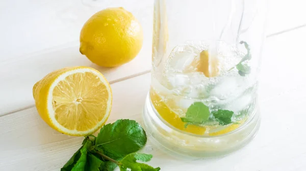 Imagen de primer plano de verter agua fría en vidrio con limones, menta y hielo — Foto de Stock