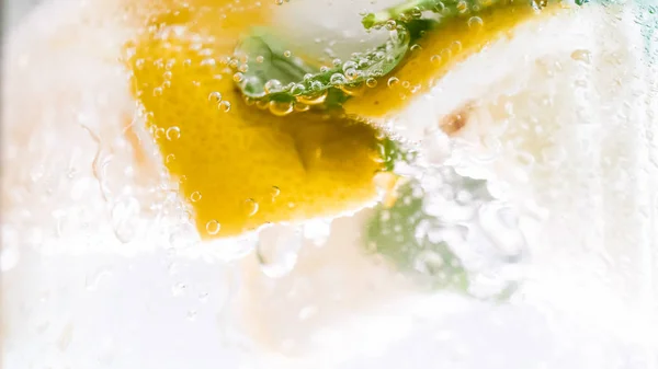 Makro fotoğraf hava baloncuklar üzerine nane yaprakları ve soğuk suda limon dilimleri — Stok fotoğraf