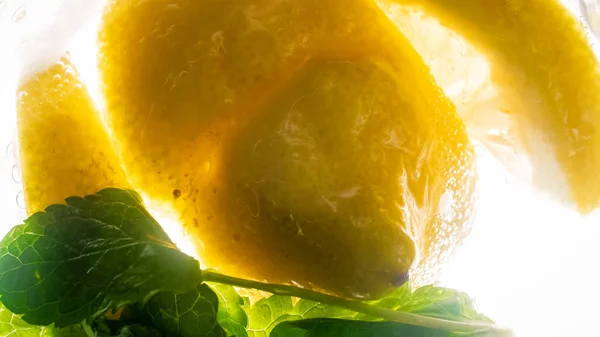 Макроподсветка изображения лимонов и листьев мяты в газированной воде — стоковое фото