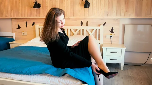 Giovane donna d'affari elegante togliersi le scarpe sul letto in camera d'albergo — Foto Stock
