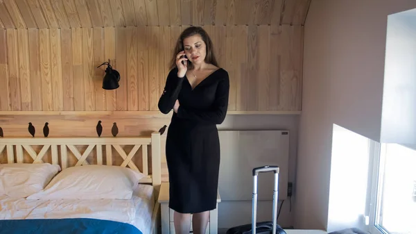 Beautiful young businesswoman walking in hotel room and talking by phone — Stock Photo, Image