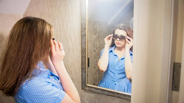 Retrato de mujer joven probándose gafas de sol frente al espejo en el baño —  Fotos de Stock