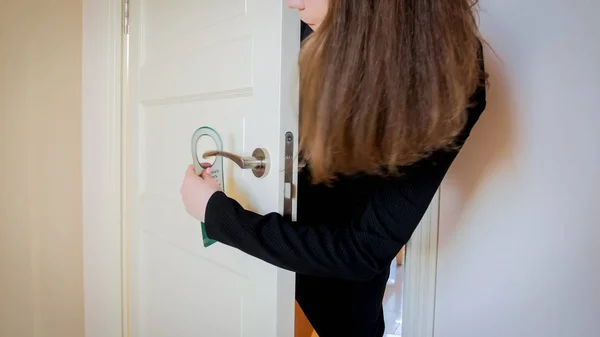 Closeup image of young woman putting do not disturb sign on door handle — Stock Photo, Image