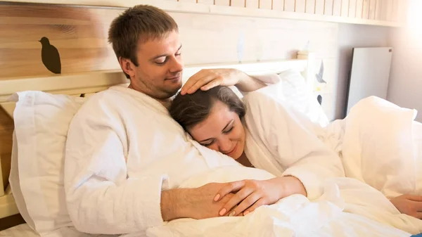 Portrai z piękną, młodą kobietę w szlafrok, przytulanie męża w łóżku — Zdjęcie stockowe