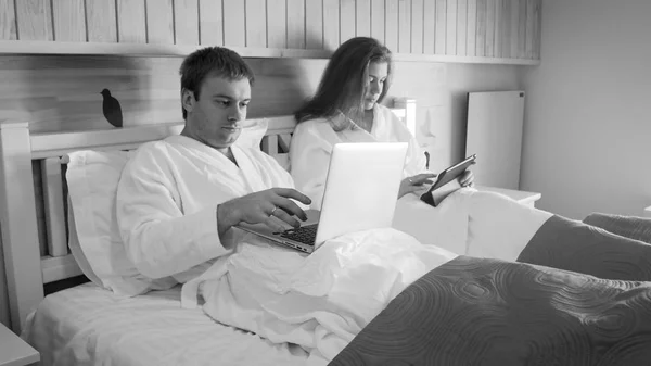 Imagen en blanco y negro de una joven pareja de empresarios que trabajan en la cama por la mañana —  Fotos de Stock