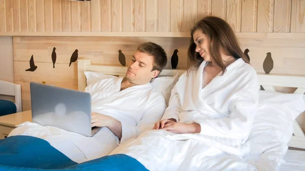 Schöne junge Frau sieht ihren Mann, der morgens am Laptop arbeitet — Stockfoto