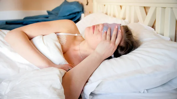 Closeup portrait of young woman with mask for sleeping lying in bed — Stock Photo, Image
