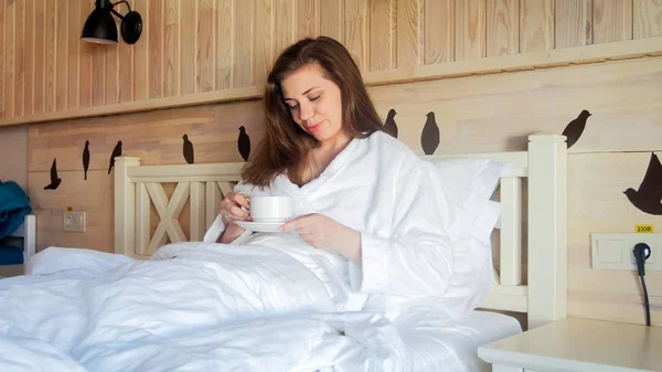 Hermosa mujer morena acostada en la cama y sosteniendo una taza de café —  Fotos de Stock