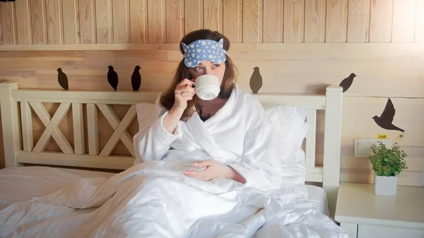 Retrato de una hermosa joven acostada en la cama por la mañana y bebiendo té — Foto de Stock