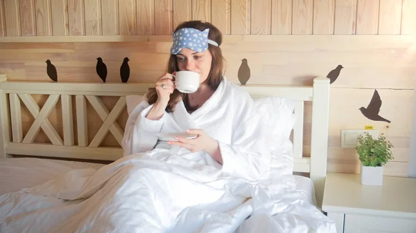 Porträt einer jungen brünetten Frau, die im Hotelzimmer Kaffee im Bett trinkt — Stockfoto
