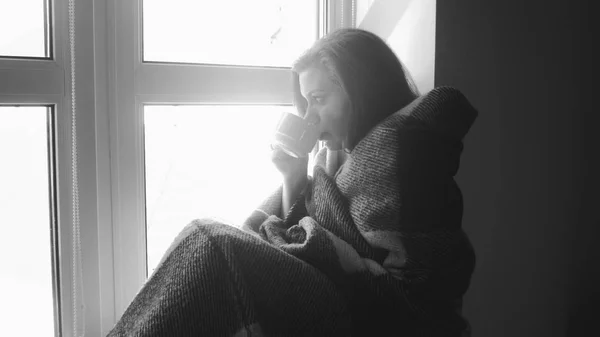 Black and white portrait of young owman in plaid drinking coffee on windowsill — Stock Photo, Image