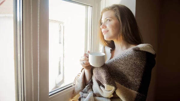Portrait tonique de jeune femme souriante en plaid regardant par la fenêtre — Photo