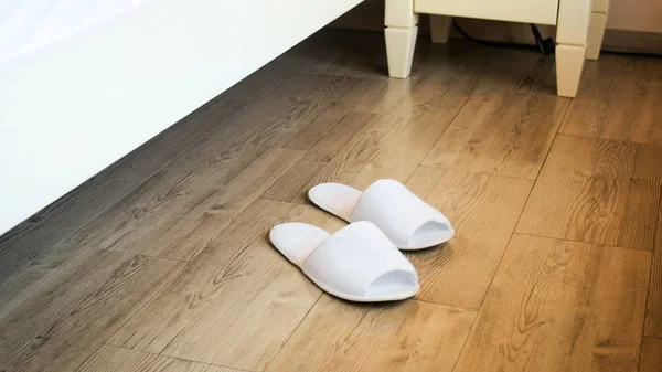 Imagen de primer plano de zapatillas blancas cerca de la cama en la habitación del hotel — Foto de Stock