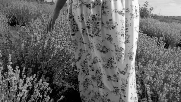 Black adn white closeup photo of young woman in dress walking at lavender field
