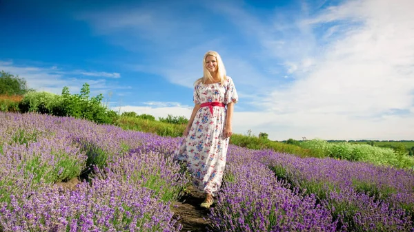 Mujer rubia feliz en vestido largo de pie en el campo de lavanda — Foto de Stock