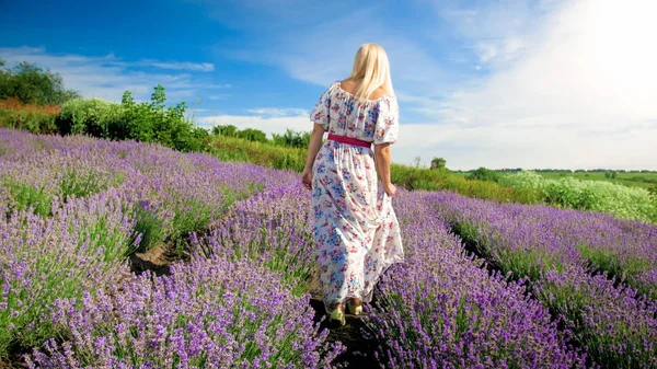 Jeune femme blonde en robe longue marchant entre les rangées de champ de lavande — Photo