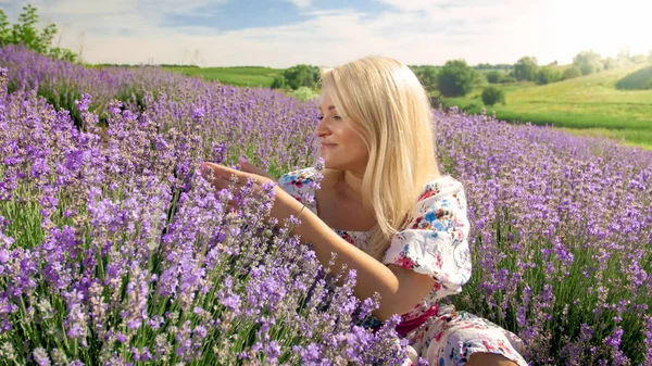 Portret van lachende jonge vrouw zit in Lavendel veld en aanraken van bloemen — Stockfoto
