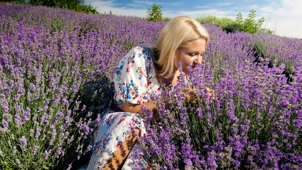 Retrato de una joven rubia sentada en el suelo en el campo de lavanda y oliendo flores — Foto de Stock