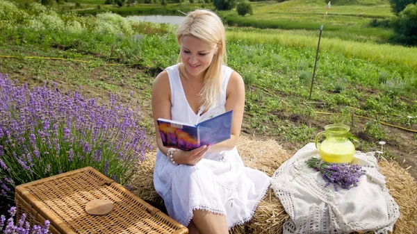 Beautiful smiling woman having picnic in field and reading book — Stock Photo, Image