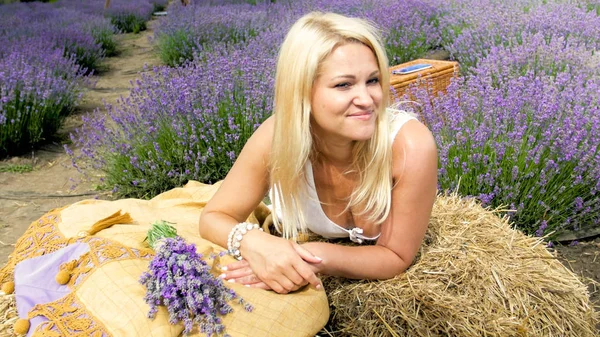 Portrait of smiling blonde woman lying on hay stack in lavender field — Stock Photo, Image