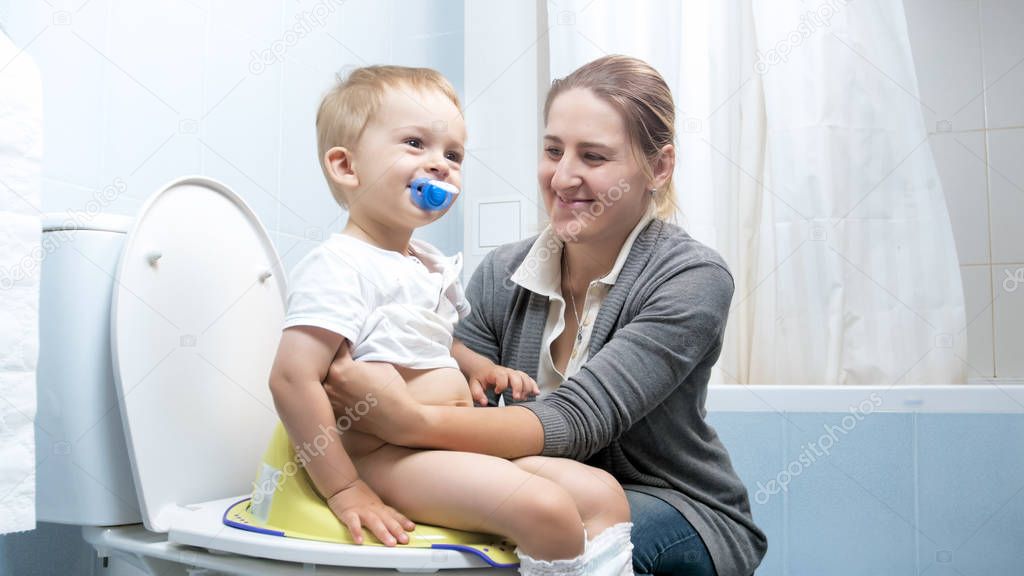 Young smiling mother with her toddler boy sitting on toilet