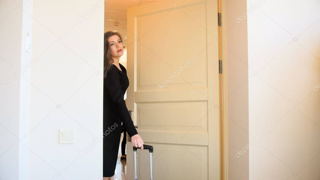 Beautiful young businesswoman with suitcase walking in hotel room